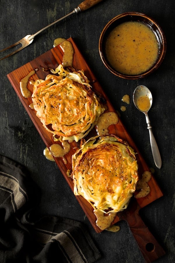 Photo of Roasted Cabbage Steaks with Mustard Vinaigrette on wood cutting board with gray striped towel.