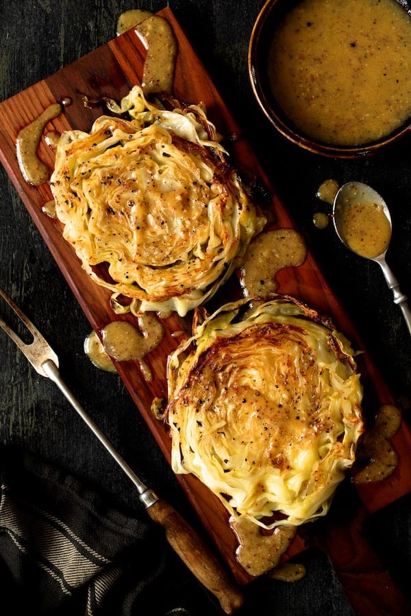 Photo of Roasted Cabbage Steaks with Mustard Vinaigrette on wood cutting board drizzled with vinaigrette.