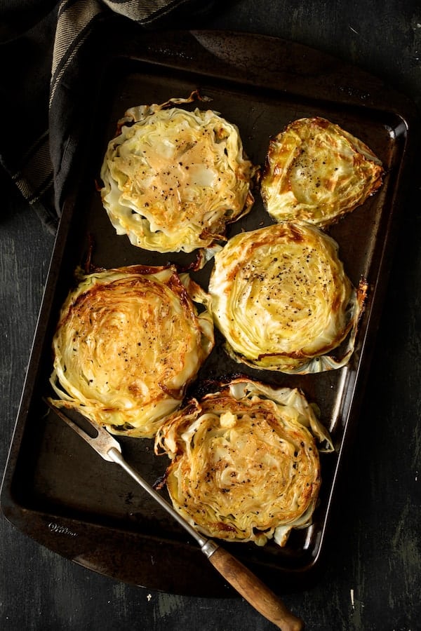 Photo of five roasted cabbage steaks on baking sheet.