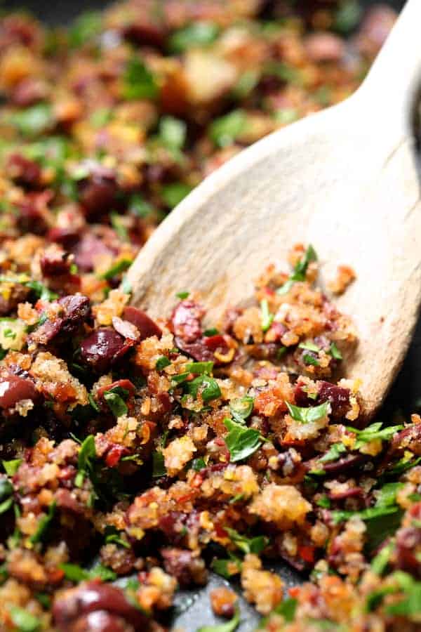 Close-up photo of breadcrumbs in pan with wooden serving spoon.