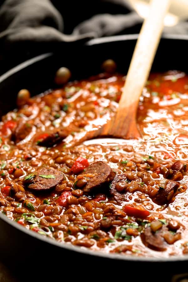 Photo of Soupy Spanish Lentils with Chorizo cooking in pot with wooden spoon.