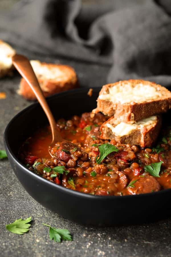 Photo of one serving of Soupy Spanish Lentils with Chorizo and Manchego Toast garnished with fresh parsley.