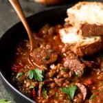Soupy Spanish Lentils with Chorizo and Manchego Toast in black bowl with copper fork.