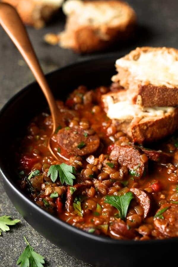 Soupy Spanish Lentils with Chorizo and Manchego Toast in black bowl with copper fork.