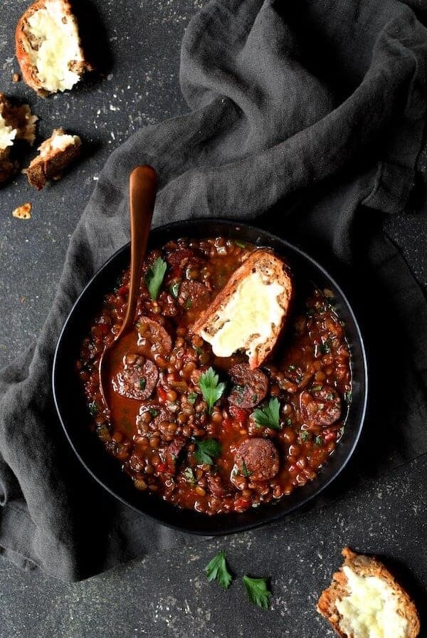 Soupy Spanish Lentils with Chorizo and Manchego Toast in black bowl and gray napkin.