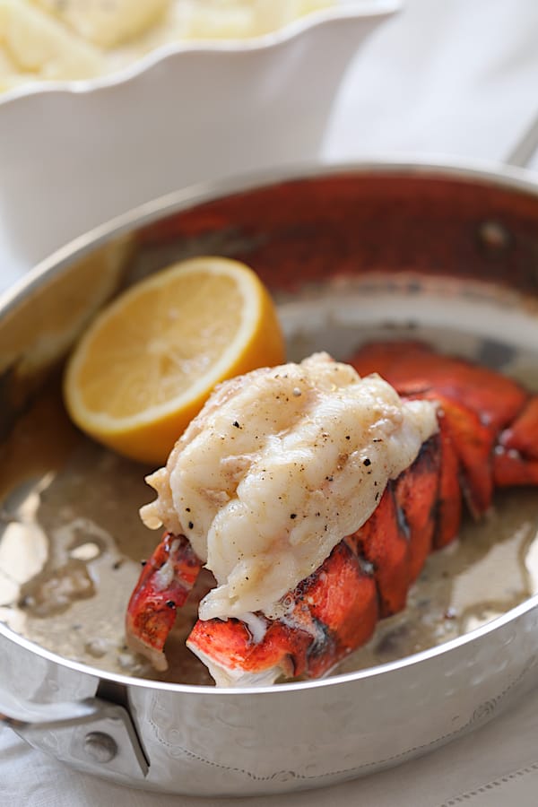 Photo of broiled lobster tail in roasting dish garnished with lemon.
