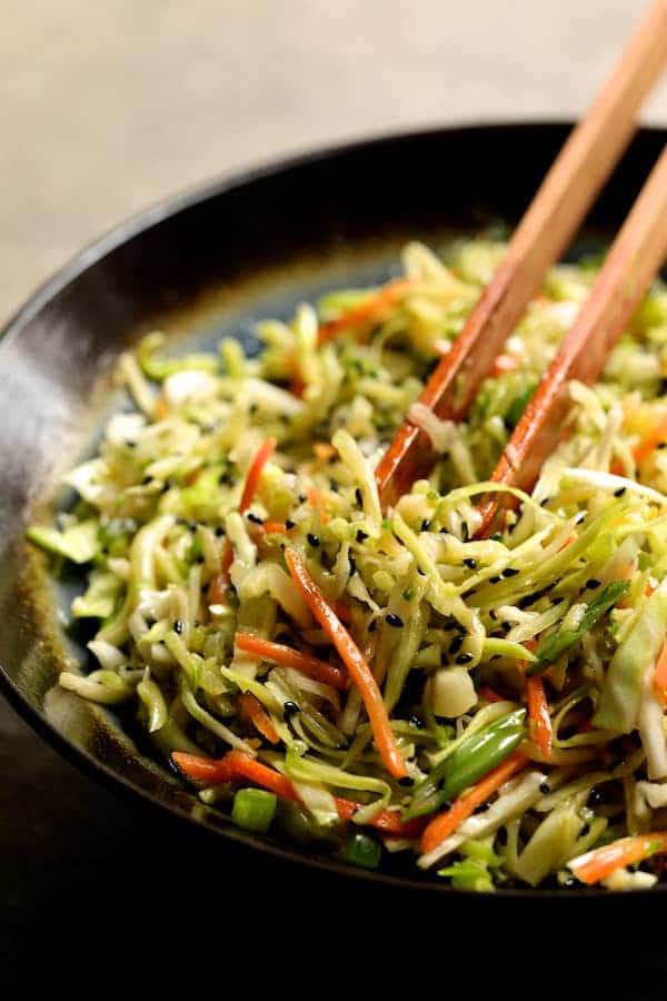 Photo of spicy slaw in bowl being stirred with tongs.