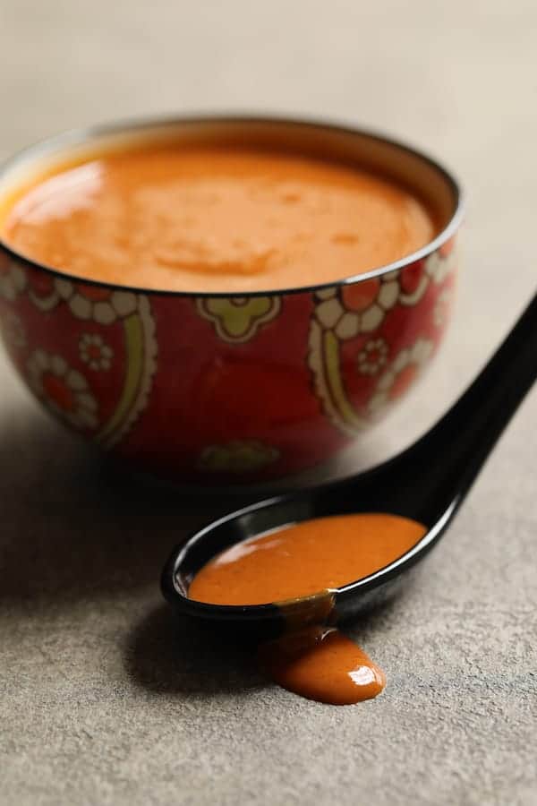Photo of Tahini Gochujang Sauce in bowl with some on a black spoon.