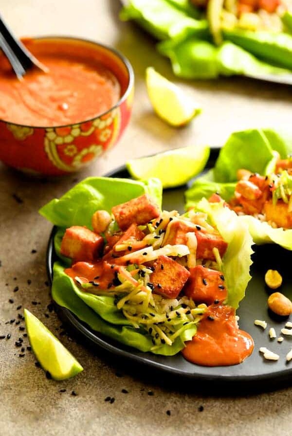 One Vegan Korean Tofu Lettuce Wrap with Tahini Gochujang Sauce and Spicy Slaw on black plate.