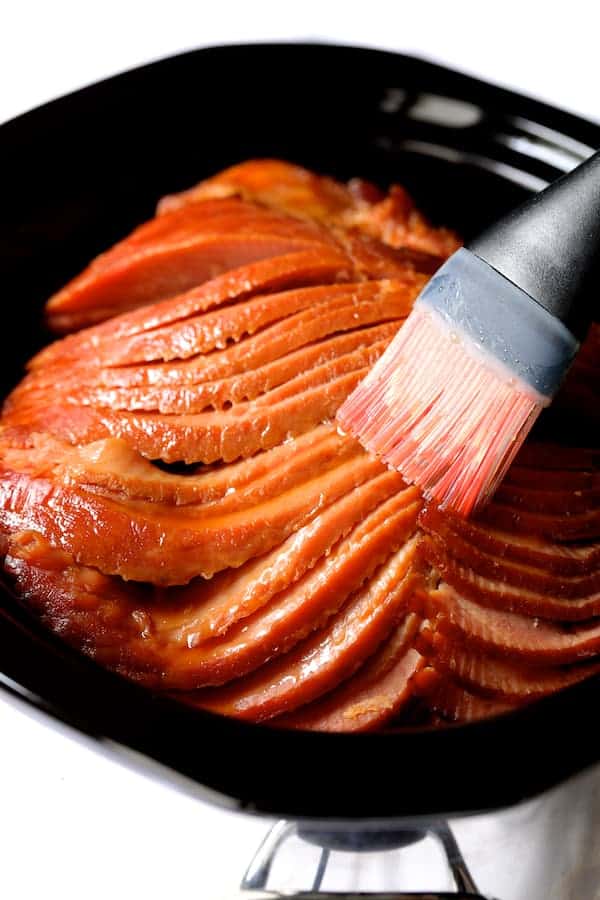 Photo of spiral ham being brushed with pastry brush in slow cooker.