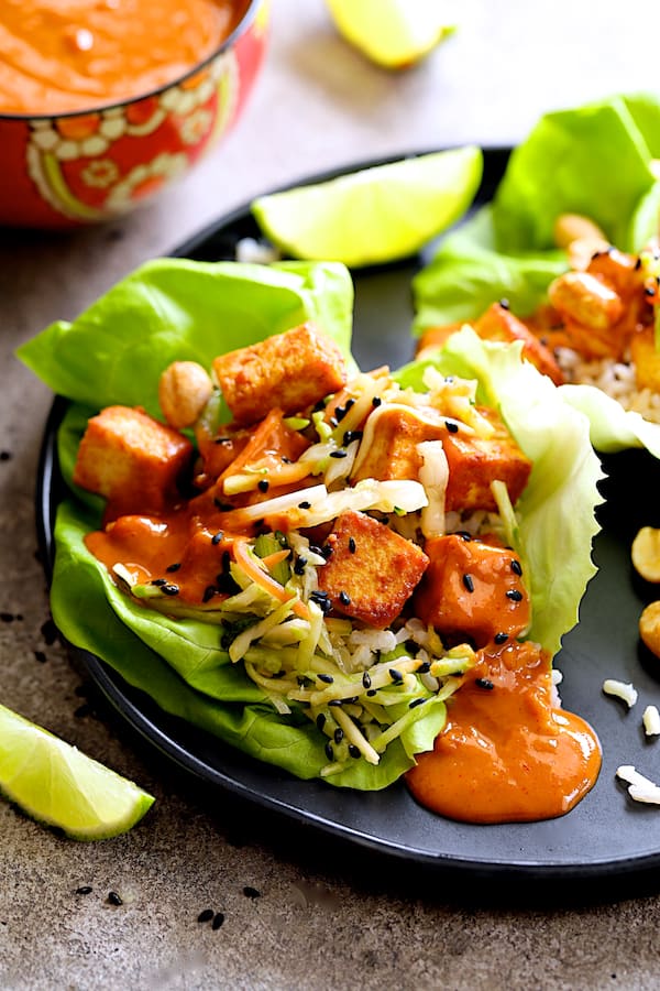 Close-up photo of Vegan Korean Tofu Lettuce Wraps with Tahini Gochujang Sauce and Spicy Slaw on black plate with lime wedges.