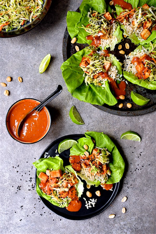 Photo of Vegan Korean Tofu Lettuce Wraps with Tahini Gochujang Sauce on platter and individual plate with lime wedges.