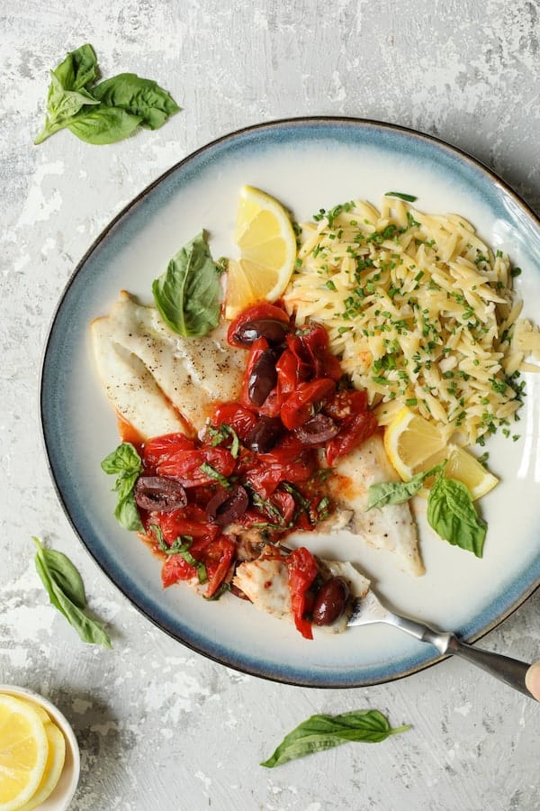 Photo of Baked Fish with Cherry Tomato Olive Sauce and Lemon Chive Asiago Orzo on blue-rimmed plate with a forkful cut from the fish.