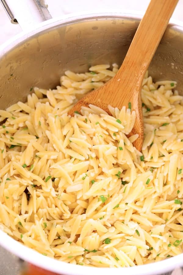 Photo of orzo in saucepan being stirred with wooden spoon.