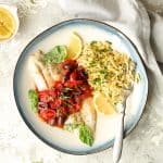 Baked Fish with Cherry Tomato and Olive Sauce and Lemon Chive Asiago Orzo hero shot on blue-rimmed plate