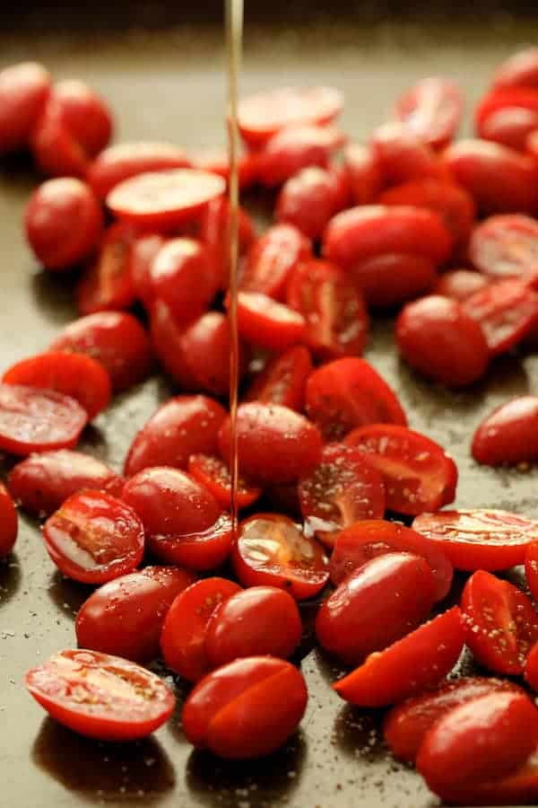 Photo of tomatoes on baking sheet being drizzled with olive oil before being roasted.