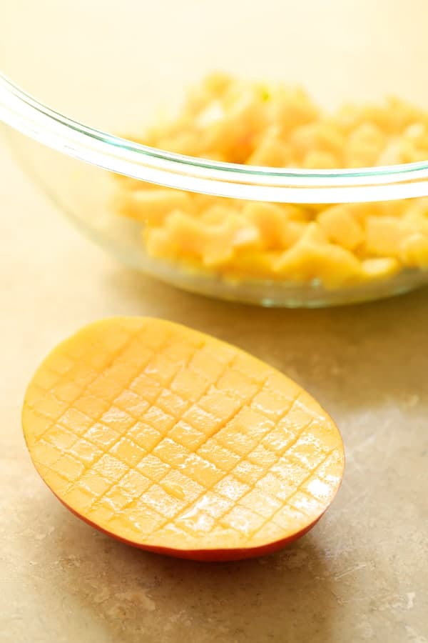 Photo showing how to easily dice a mango with some in glass bowl already diced.