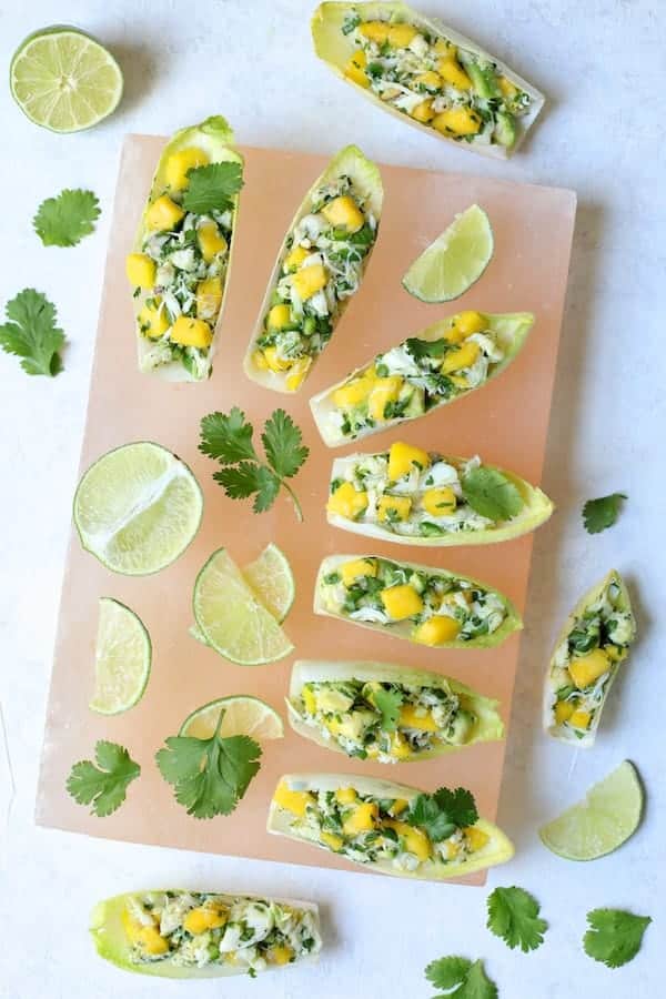 Photo of Crab Mango and Avocado Salad with Chile Lime Dressing in Endive on pink salt block.