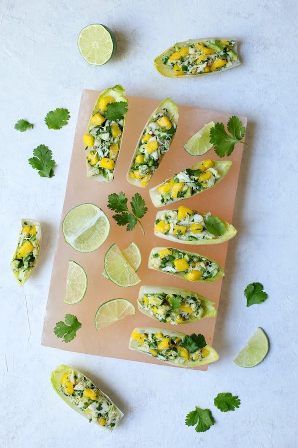 Photo of Crab Mango and Avocado Salad with Chile Lime Dressing in Endive on pink salt block garnished with limes and cilantro.