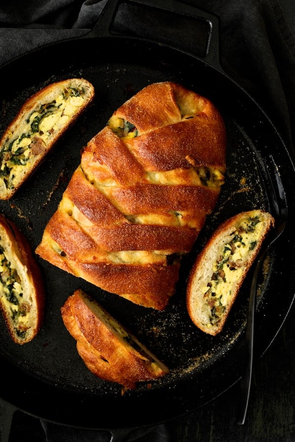 Photo of Savory Breakfast Strudel with Eggs Sausage and Swiss Chard cut into pieces in cast iron pan.