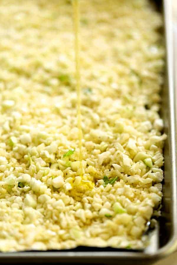 Photo of cauliflower rice being drizzled with oil on sheet pan before roasting.