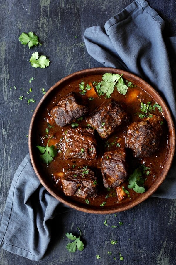 Photo of Slow Cooker Beef Short Ribs Barbacoa with Cilantro Lime Cauliflower Rice in clay serving bowl on blue background with blue napkin.