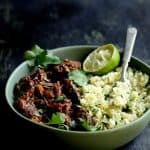 Slow Cooker Beef Short Ribs Barbacoa with Cilantro Lime Cauliflower Rice - Close-up in green serving bowl garnished with cilantro and lime