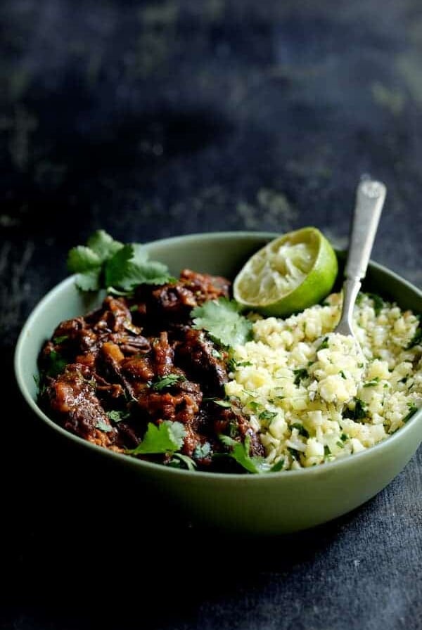 Slow Cooker Beef Short Ribs Barbacoa with Cilantro Lime Cauliflower Rice - Close-up in green serving bowl garnished with cilantro and lime