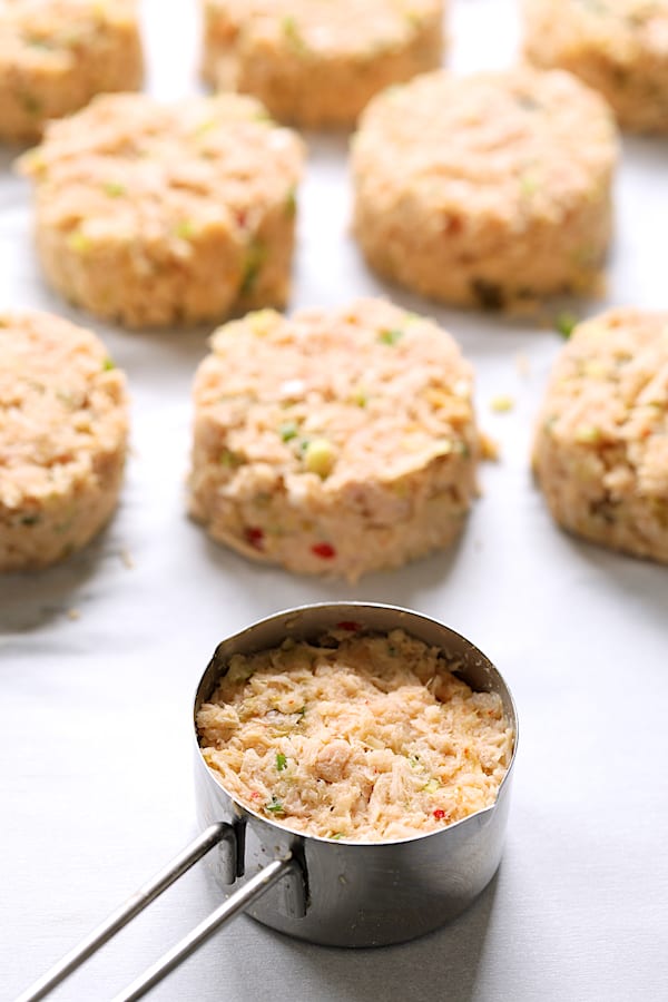 Photo of tuna cake mixture in measuring cup with formed cakes in the background.