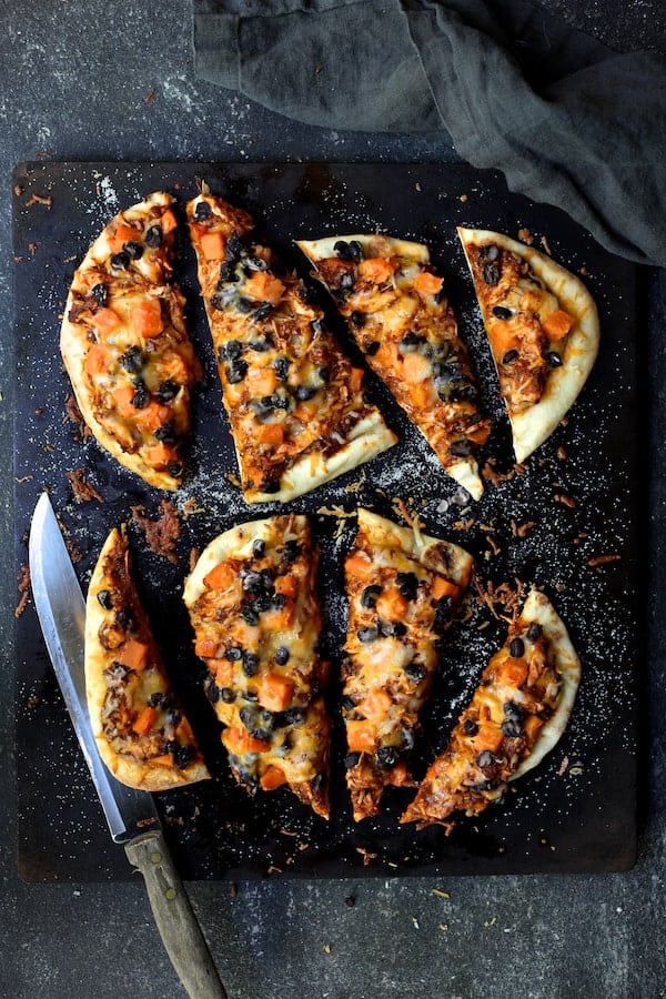 Photo of Chipotle Chicken Sweet Potato and Black Bean Flatbread Pizzas on pizza stone cut into four pieces.