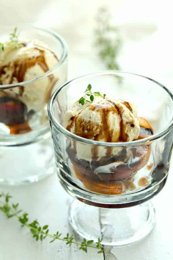 Photo of Grilled Peaches with Vanilla Ice Cream and Honey Balsamic Drizzle in glass serving dish garnished with fresh thyme.