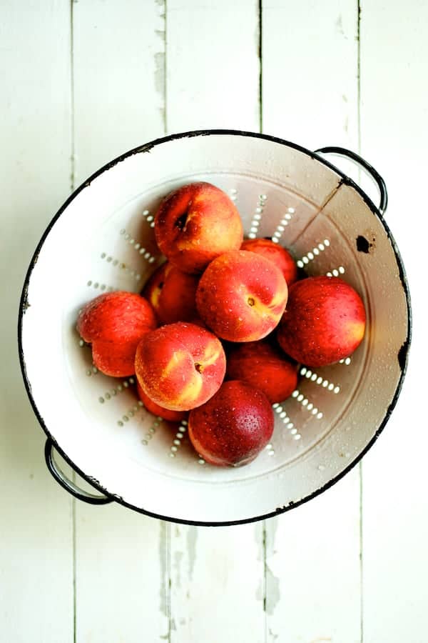 Photo of freshly washed peaches in white colander.