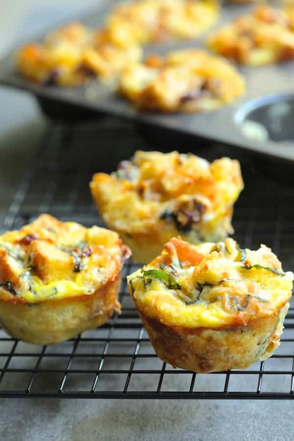 Photo of three Muffin Pan Stratas with Basil and Sun-Dried Tomatoes on cooling rack with remainder still in the pan in the background.