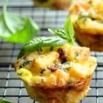 Muffin Pan Stratas with Basil and Sun Dried Tomatoes close-up on cooling rack garnished with fresh basil.