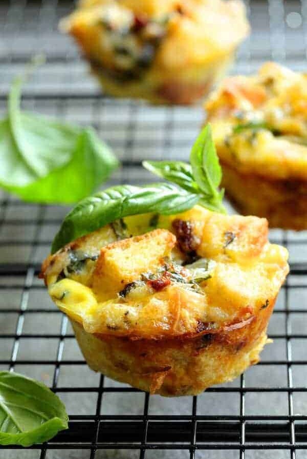 Muffin Pan Stratas with Basil and Sun Dried Tomatoes close-up on cooling rack garnished with fresh basil.