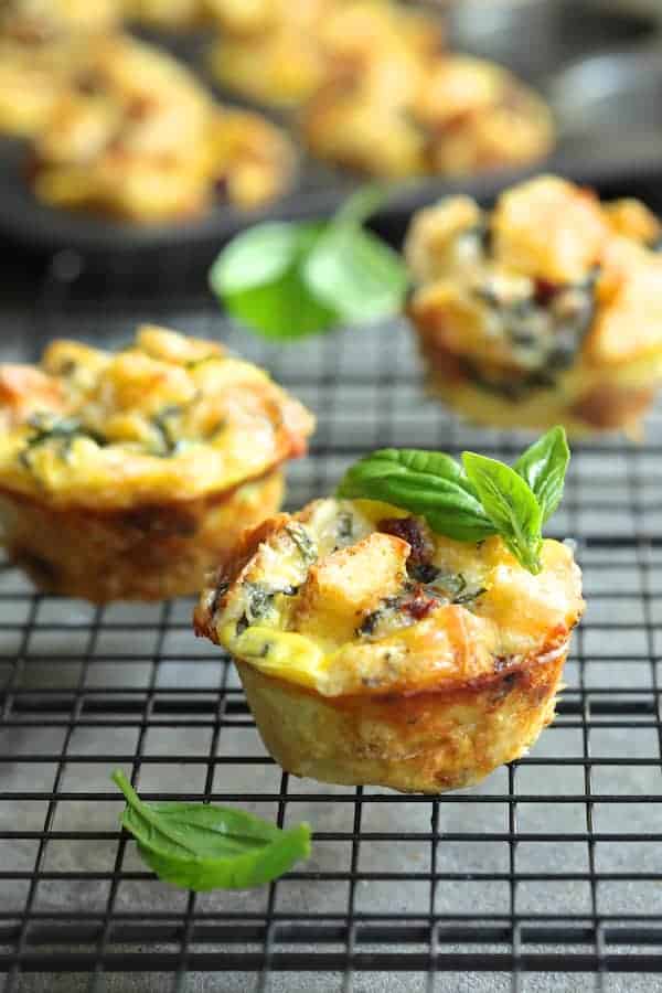 Photo of Muffin Pan Stratas with Basil and Sun-Dried Tomatoes on cooling rack garnished with fresh basil.