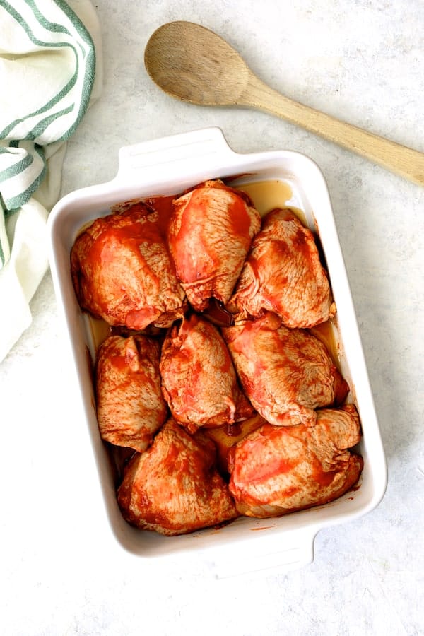 Photo of 8 raw chicken thighs in marinade in white dish ready to be battered and fried.