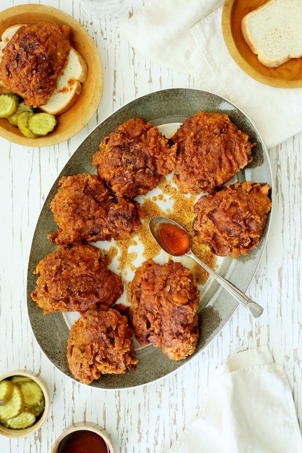 Photo of Nashville Style Hot Fried Chicken on gray-rimmed platter with accompaniments: White bread, pickles and sauce.