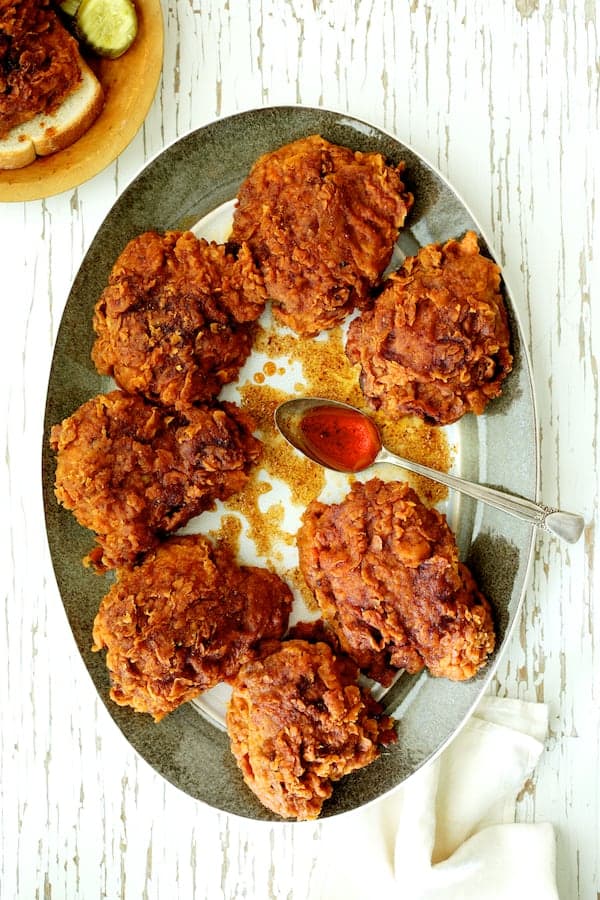 Photo of Nashville Style Hot Fried Chicken on gray rimmed platter drizzled with sauce.