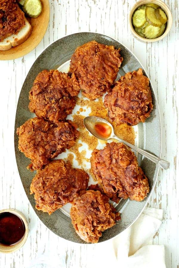 Photo of Nashville Style Hot Fried Chicken on gray rimmed platter drizzled with hot sauce.