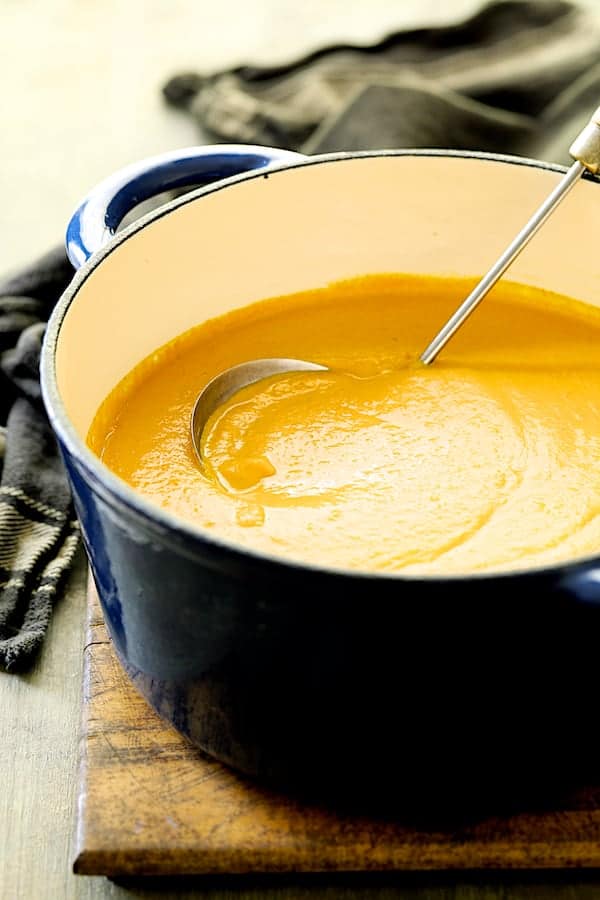 Photo of Spicy Indonesian Vegan Carrot Almond Soup in blue Dutch oven with soup ladle.