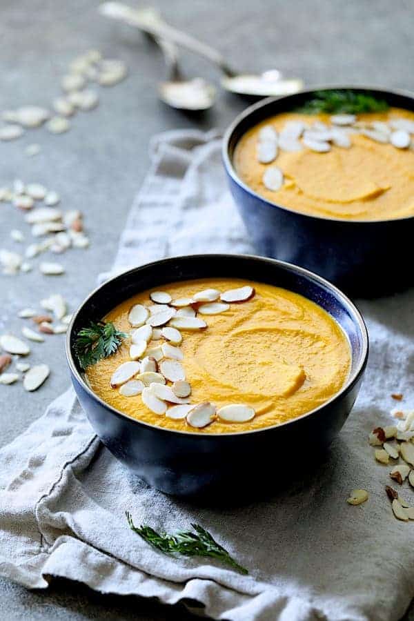 Photo of Spicy Indonesian Vegan Carrot Almond Soup in black bowls on gray napkins garnished with sliced almonds.