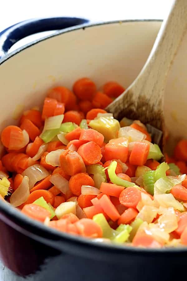 Photo of carrots and other vegetables being cooked and stirred in Dutch oven.
