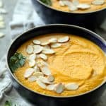 Spicy Indonesian Vegan Carrot Almond Soup closeup garnish with a carrot top sprig and sliced almonds.