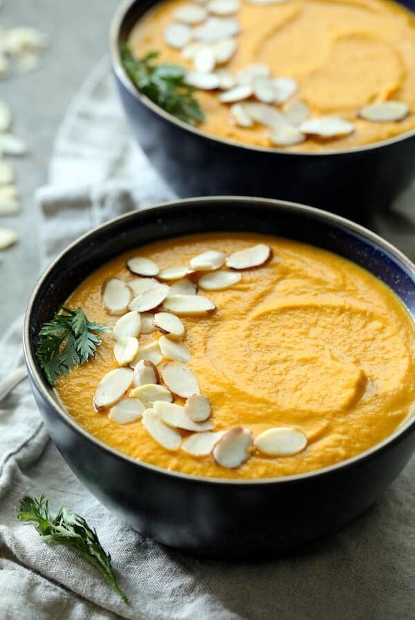 Spicy Indonesian Vegan Carrot Almond Soup closeup garnish with a carrot top sprig and sliced almonds.
