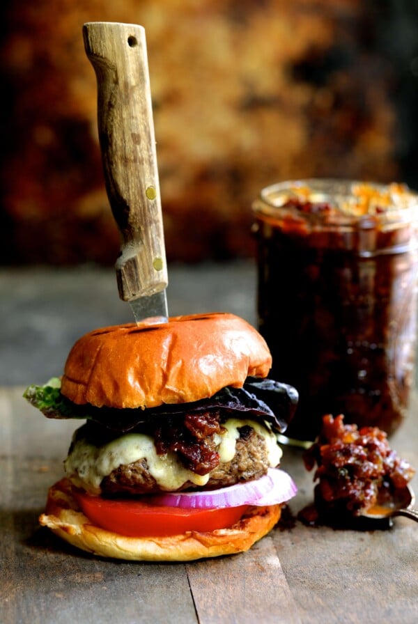 Grilled Burgers with Bacon Tomato Jam and Smoked Gouda with a steak knife through the burger and the jar of jam.