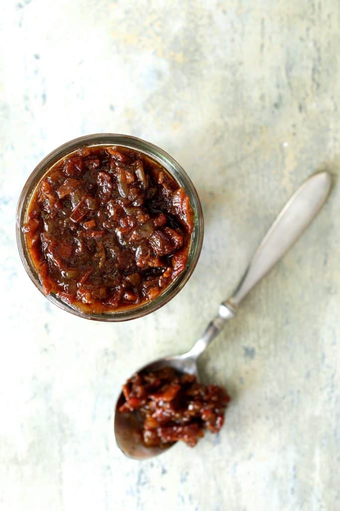 Photo of finished bacon tomato jam in glass jar with some on a spoon.
