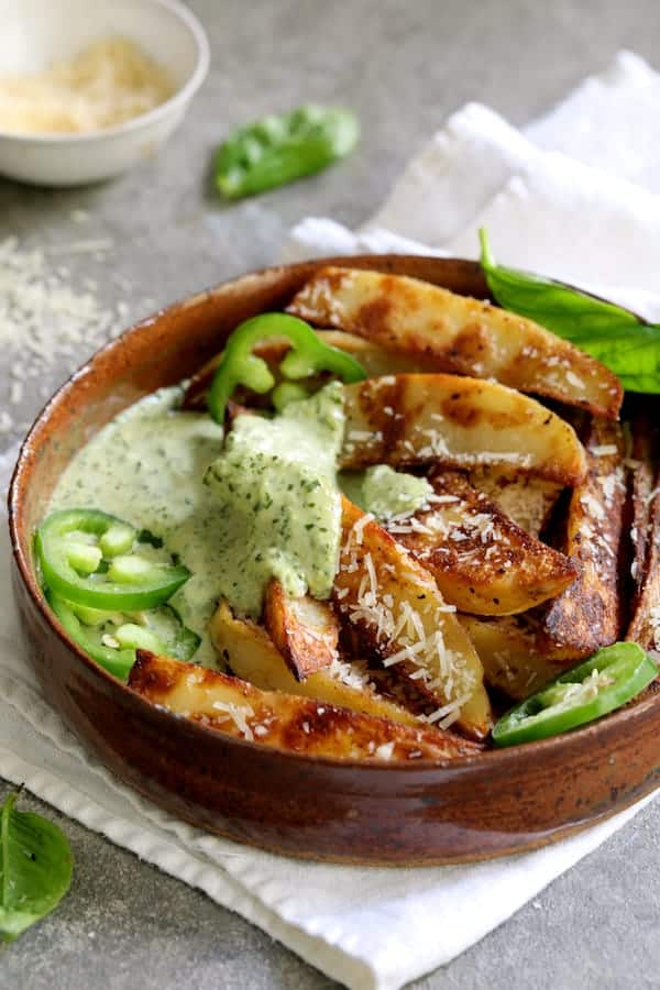 Photo of individual serving of fries with aioli garnished with jalapeno slices and fresh basil.