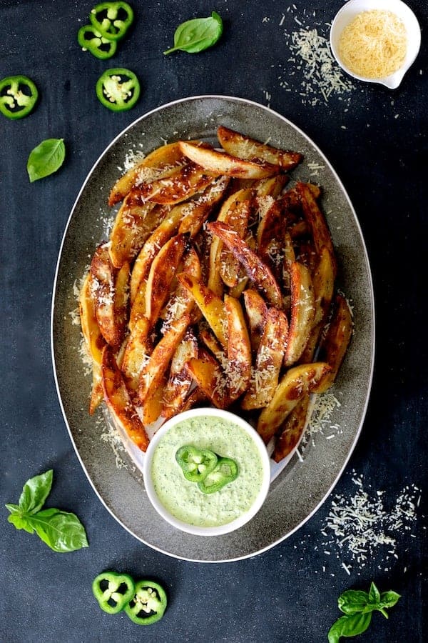 Photo of Oven Fries with Spicy Pesto Aioli on gray-rimmed platter garnished with jalapeno slices, basil leaves and Parmesan cheese.