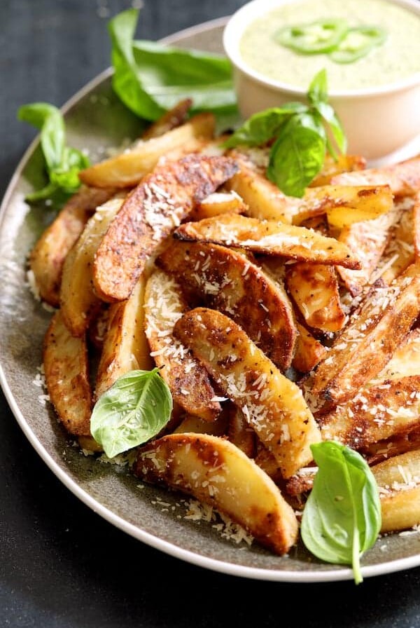 Oven Fries with Spicy Pesto Aioli on gray-rimmed platter garnished with fresh basil leaves.
